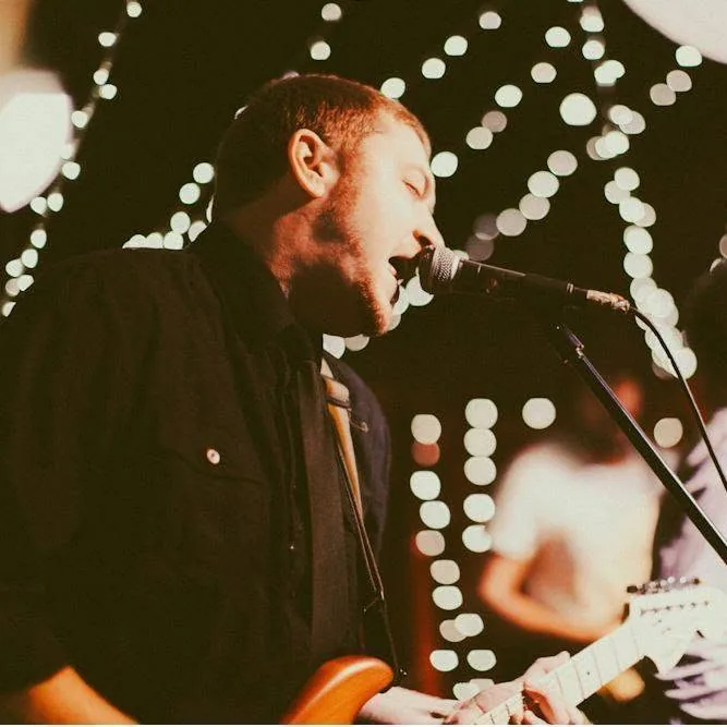 Terence singing and playing guitar on stage under string lights